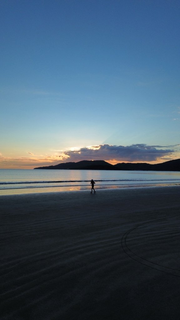 Amanhecer em Balneário Perequê com uma pessoa correndo na praia, simbolizando qualidade de vida e bem-estar à beira-mar.